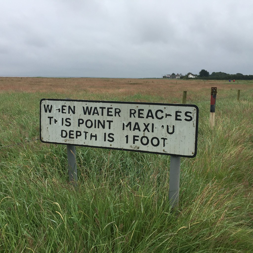 Flood depth warning sign in a grassy floodplain, a reminder for International Day for Disaster Risk Reduction