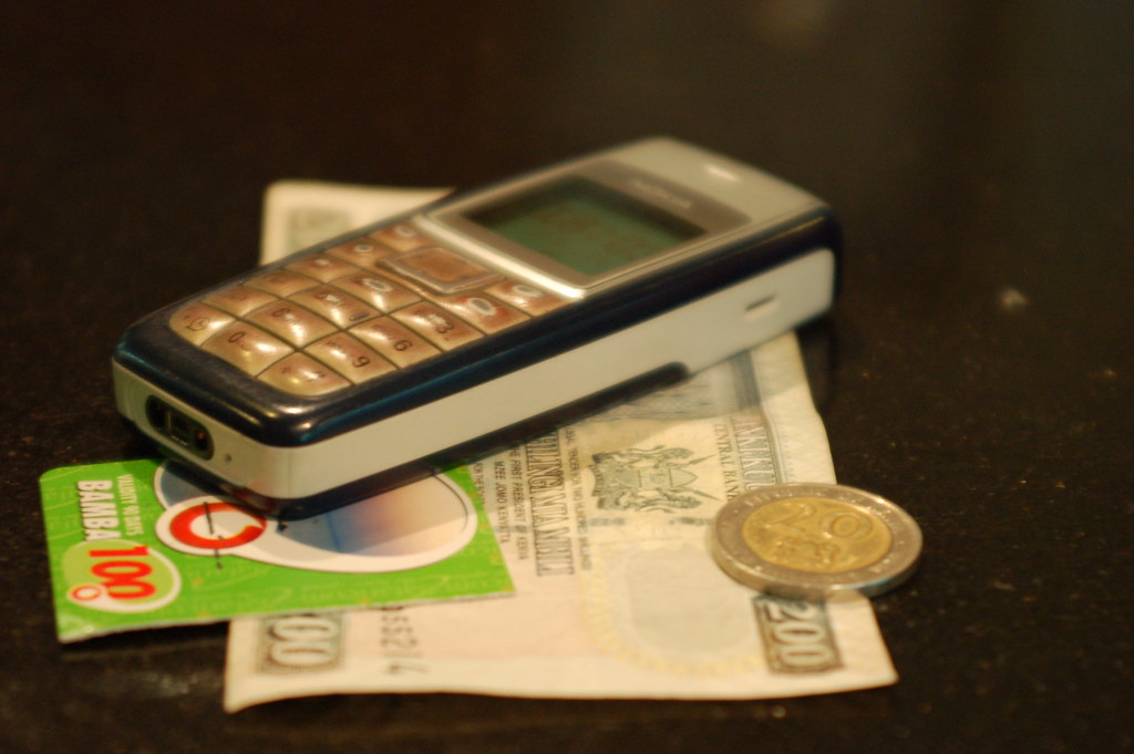 Hand holding a mobile phone and Kenyan shilling notes for an M-Pesa donation