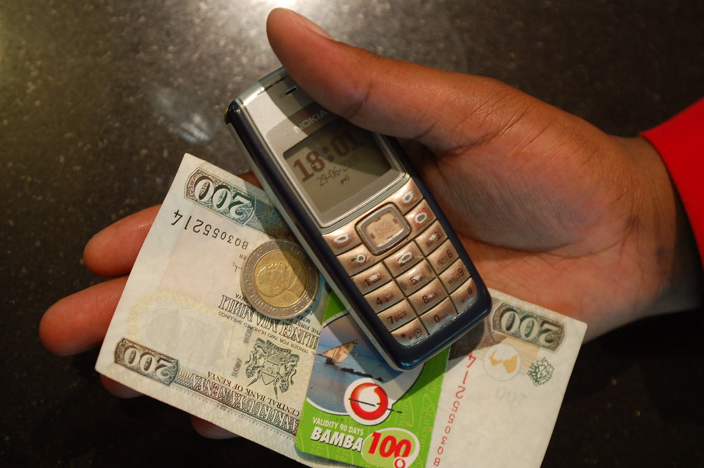Hand holding mobile phone and Kenyan shillings, representing cash transfer payments for poverty alleviation